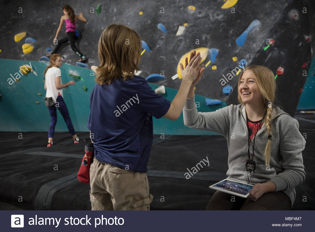Female instructor highfiving girl rock climbing student at climbing