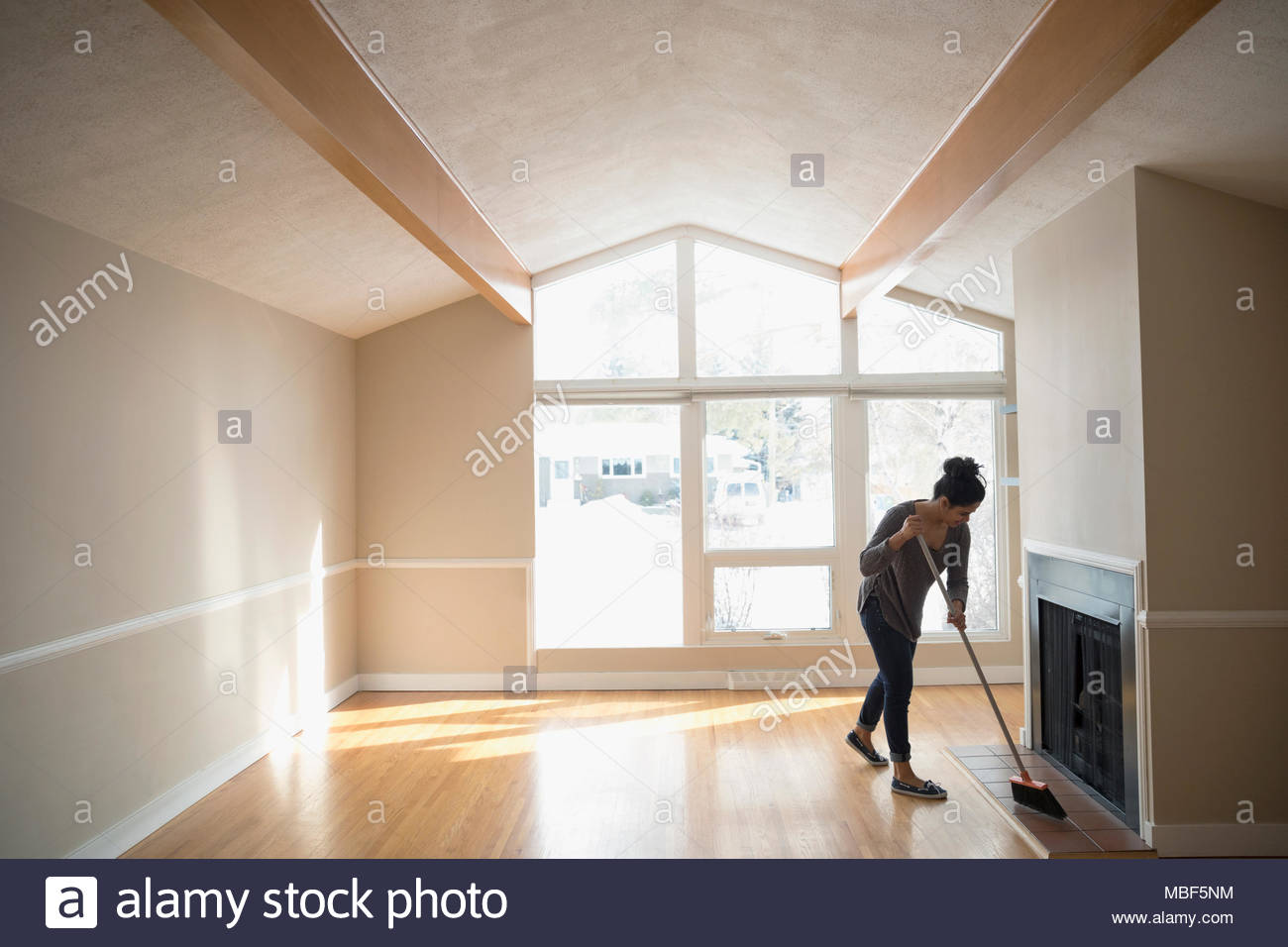 Young woman moving out, sweeping empty living room Stock Photo