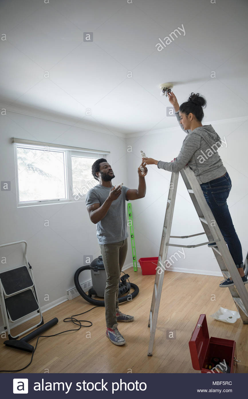 Young couple moving in, replacing light bulb with eco-friendly LED bulb, DIY Stock Photo