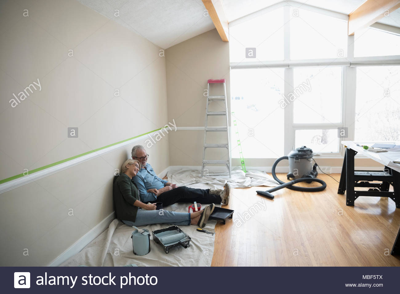 Affectionate senior couple taking a break from painting living room, DIY Stock Photo