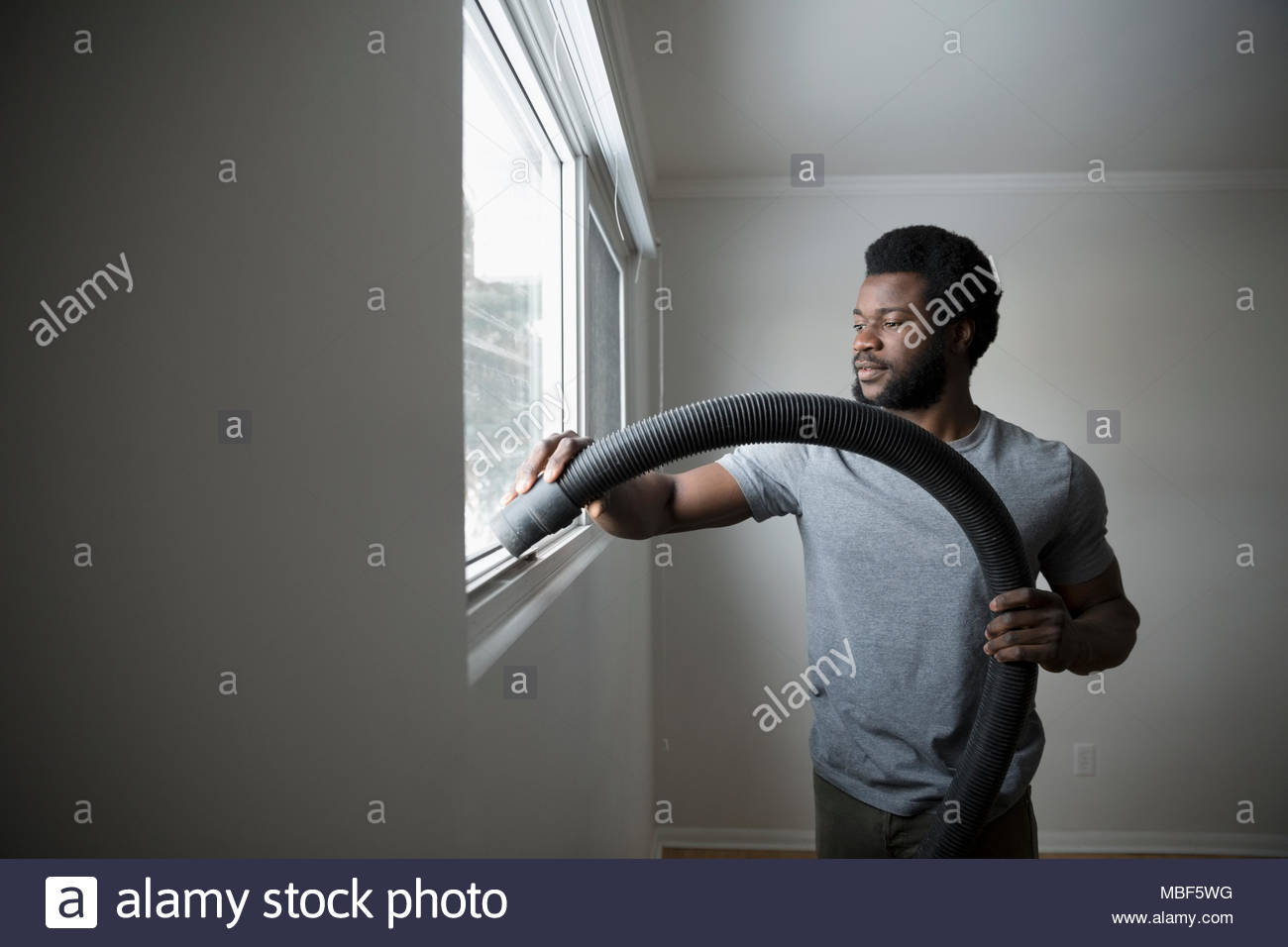 Young man moving out, cleaning and vacuuming window sill, DIY Stock Photo