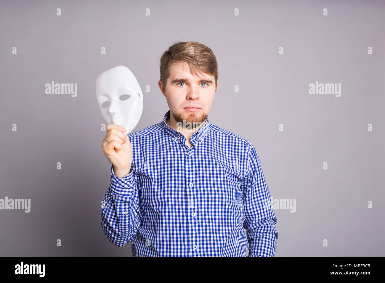 young man taking off plain white mask revealing face, gray background ...