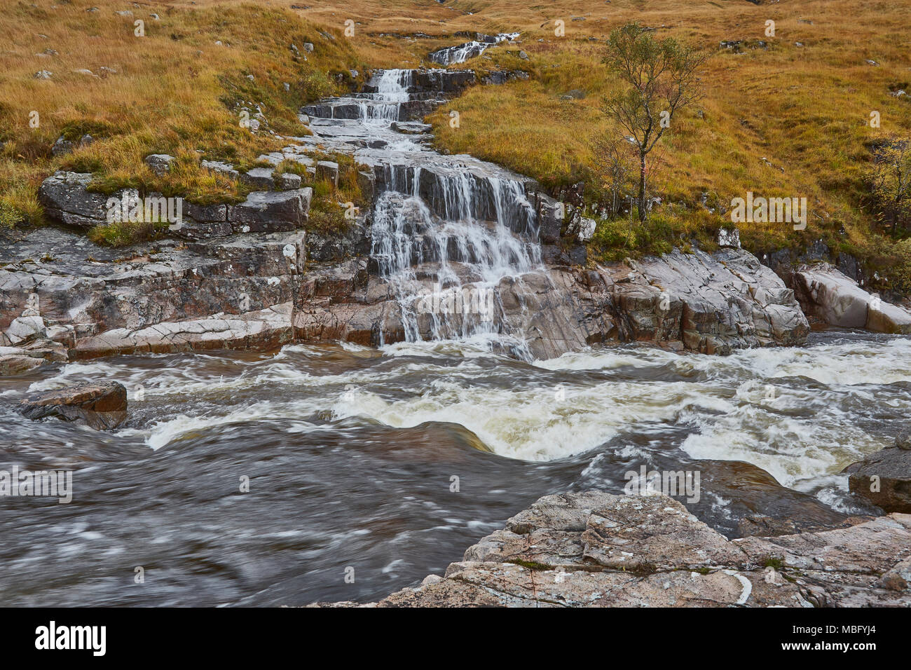 A stream of water flowing over rocks into a fast moving river below, Scottish Highlands, Scotland, UK Stock Photo