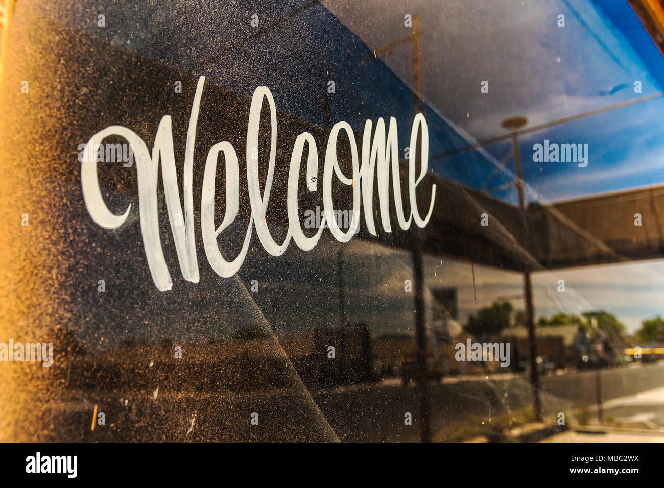 A dirty and grungy window with Welcome written on it and with the reflection on the street on a beautiful day of summer, Arizona. Hospitality concept. Stock Photo