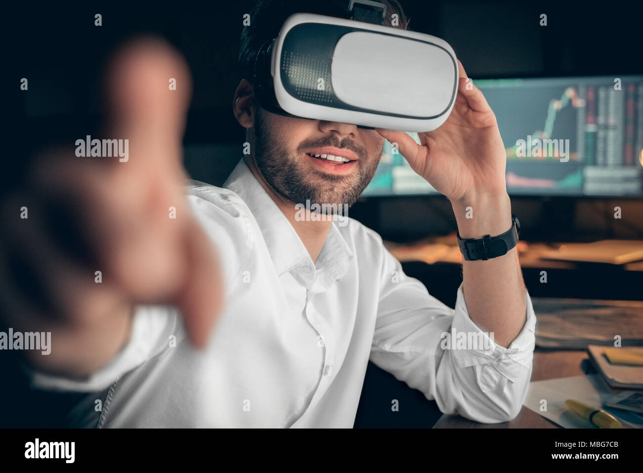 Smiling businessman wearing vr glasses touching ar interface pointing finger at camera, happy trader trading online with app in headset goggles, stock Stock Photo
