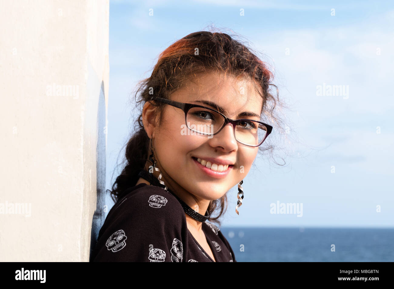 Portrait of an attractive and young woman (mixed ethnicities of Caucasian and Nepalese) wearing glasses and smiling at the ocean. Stock Photo