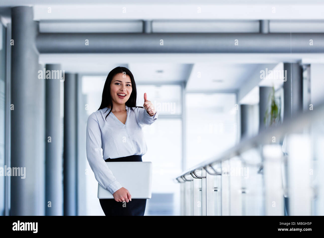 Attractive and smiling woman showing thumbs up while holding laptop in ...