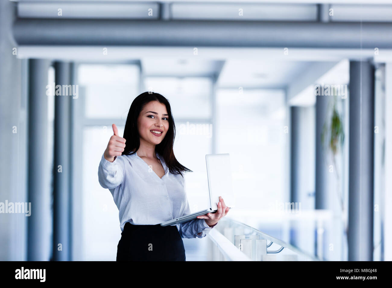 Attractive and smiling woman showing thumbs up while holding laptop in ...