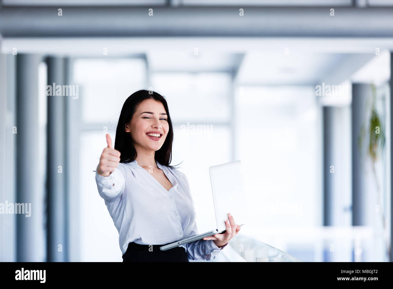 Attractive and smiling woman showing thumbs up while holding laptop in ...