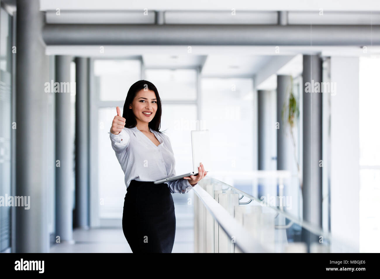 Attractive and smiling woman showing thumbs up while holding laptop in ...