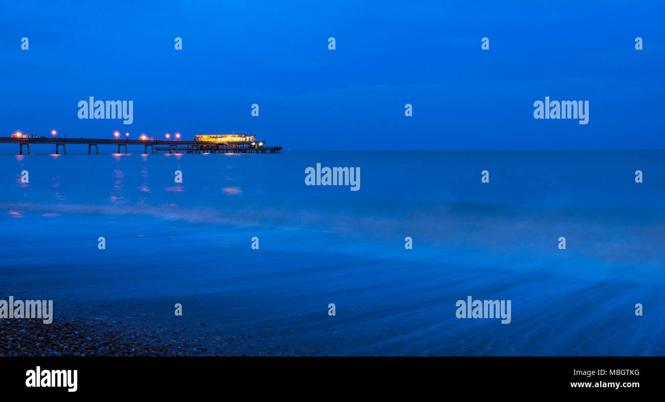 Waves crashing along Deal seafront at dusk with Deal Pier illuminated in the background. Stock Photo