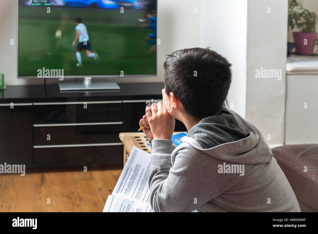 UK-Schoolboy ,10 years old ,trying to study while watching football match on TV Stock Photo