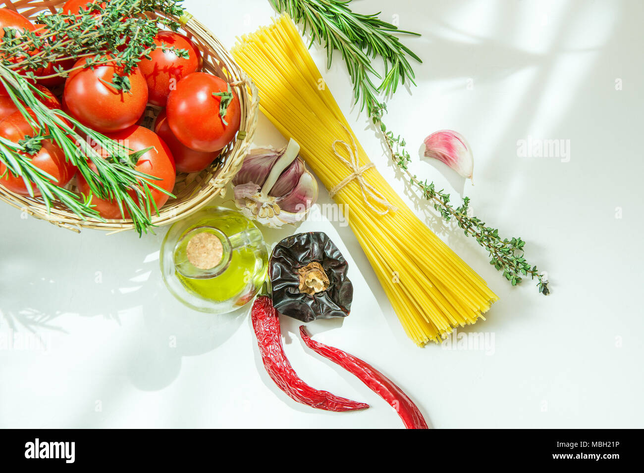 Ripe Organic Tomatoes Herbs Rosemary Thyme in Wicker Basket. Spaghetti Olive Oil in Bottle Hot Peppers Garlic on White Stone Concrete Kitchen Table. S Stock Photo