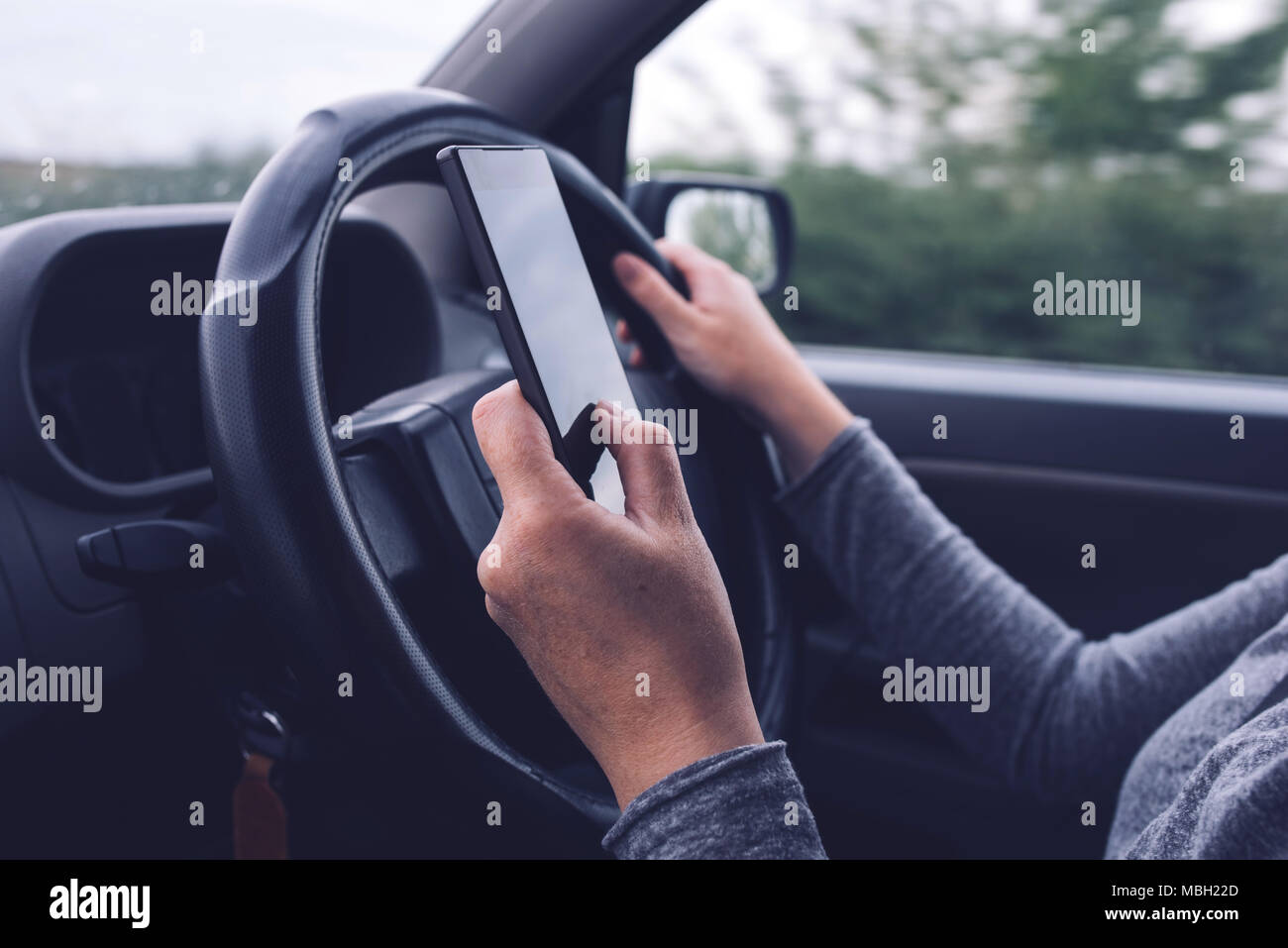 Woman simultaneously driving car and typing text message, mobile smart phone in female hands over vehicle steering wheel Stock Photo
