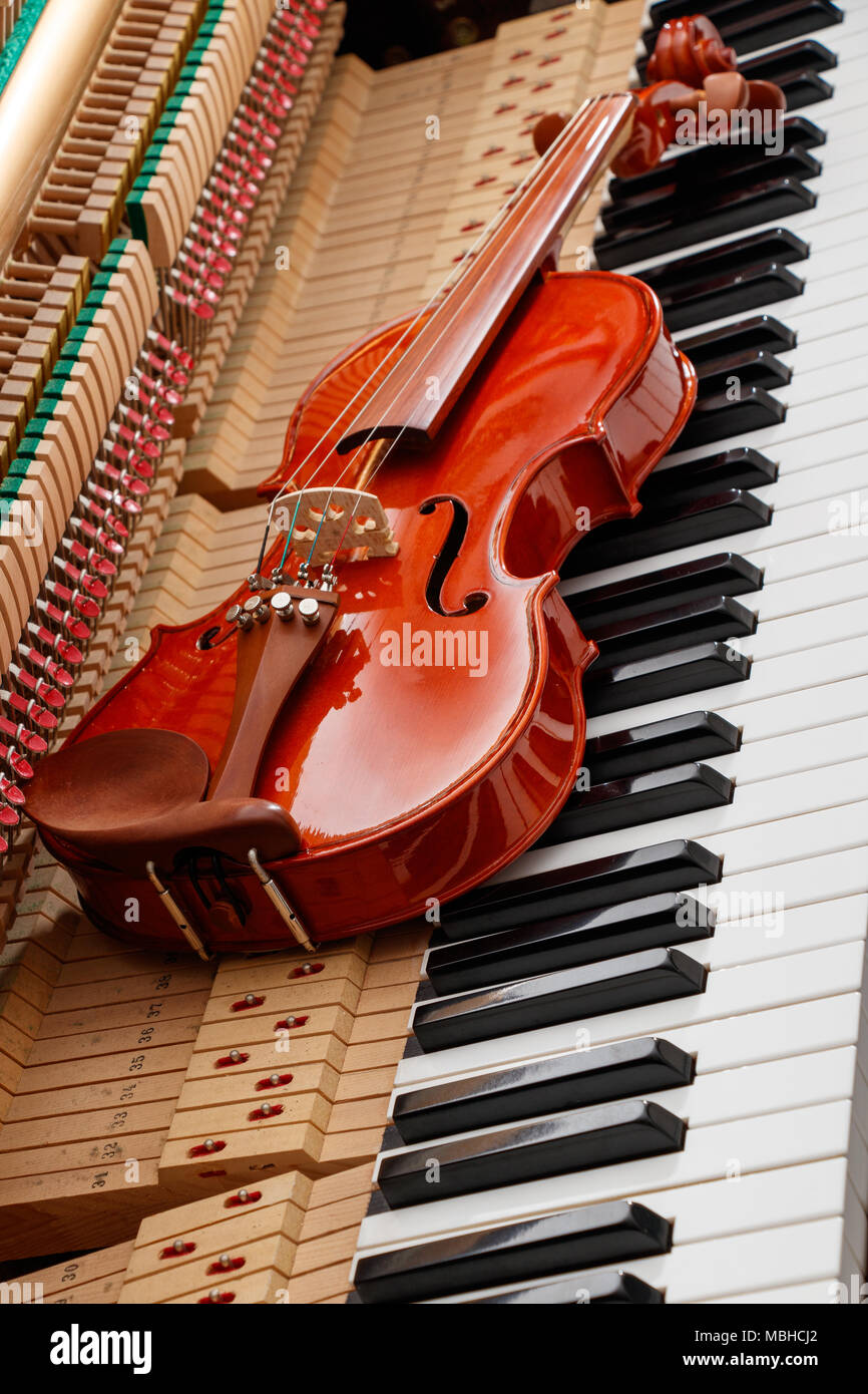 classic brown violin on the close up image of grand piano keys and interior showing strings, hammer and structure background Stock Photo