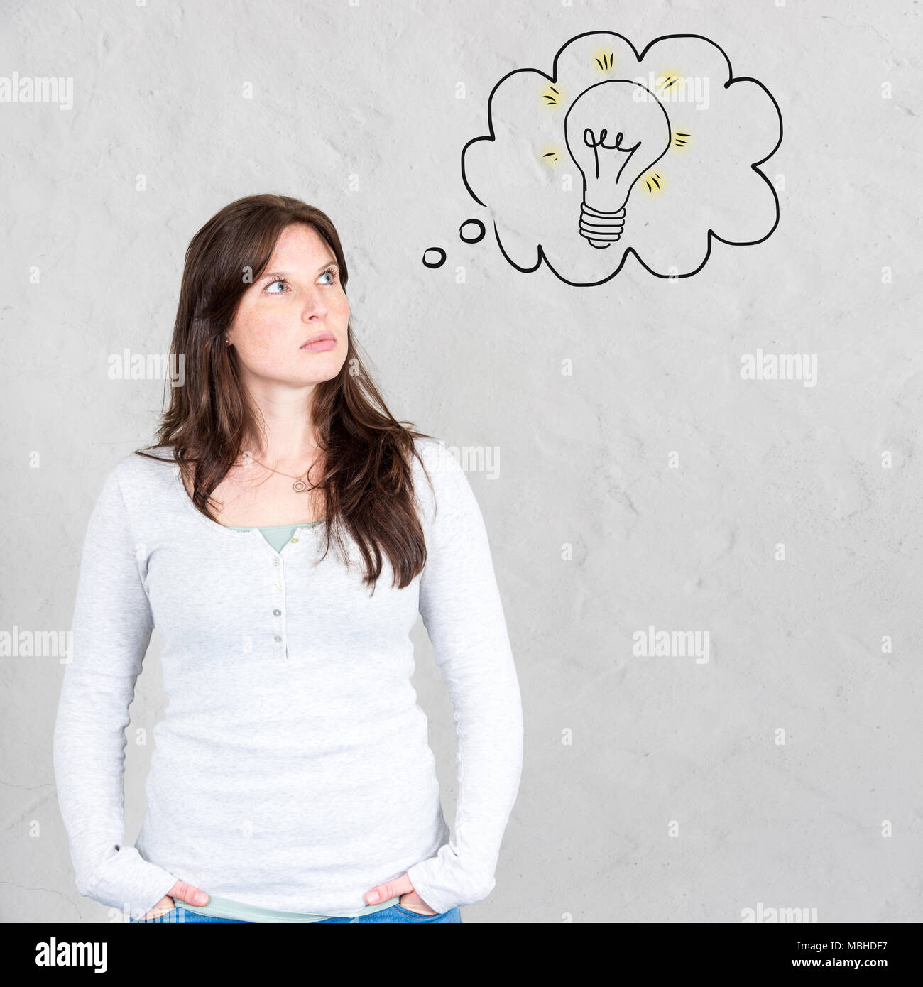 Thoughtful young woman with hands in pockets thinking about an idea and solution for a problem symbolized by light bulb in thought bubble Stock Photo