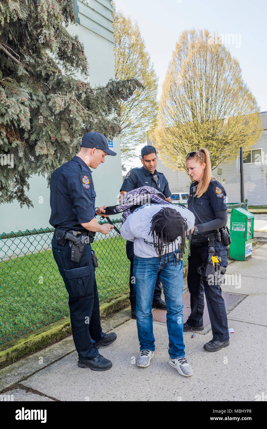 Black man with dreads being arrested on the street by Vancouver Police Officers, Vancouver, British Columbia, Canada. Stock Photo