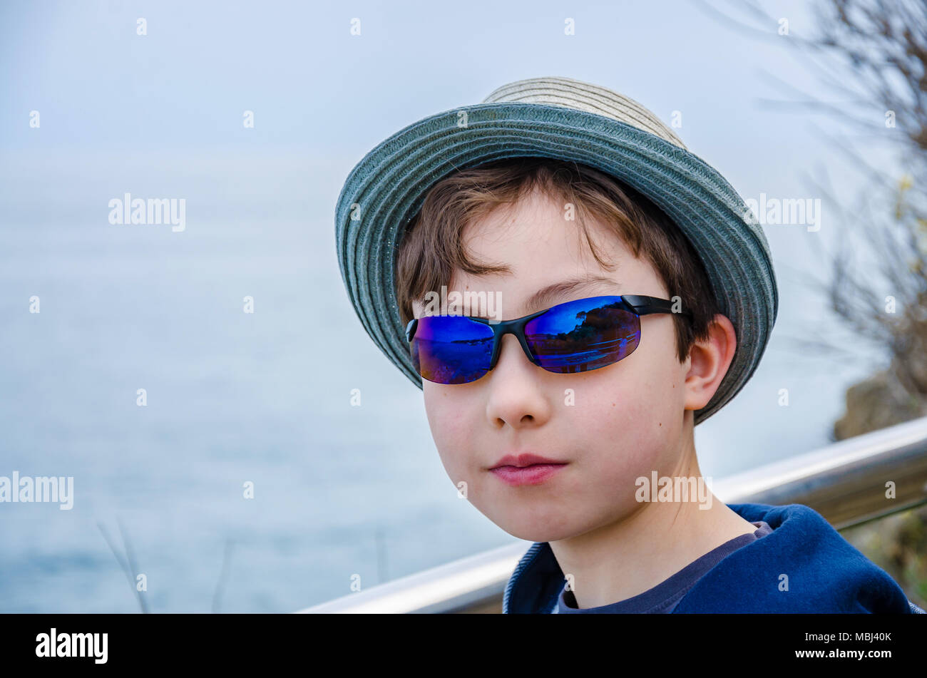 A portrait of an 8 year old boy wearing sunglasses and a sun hat. Stock Photo