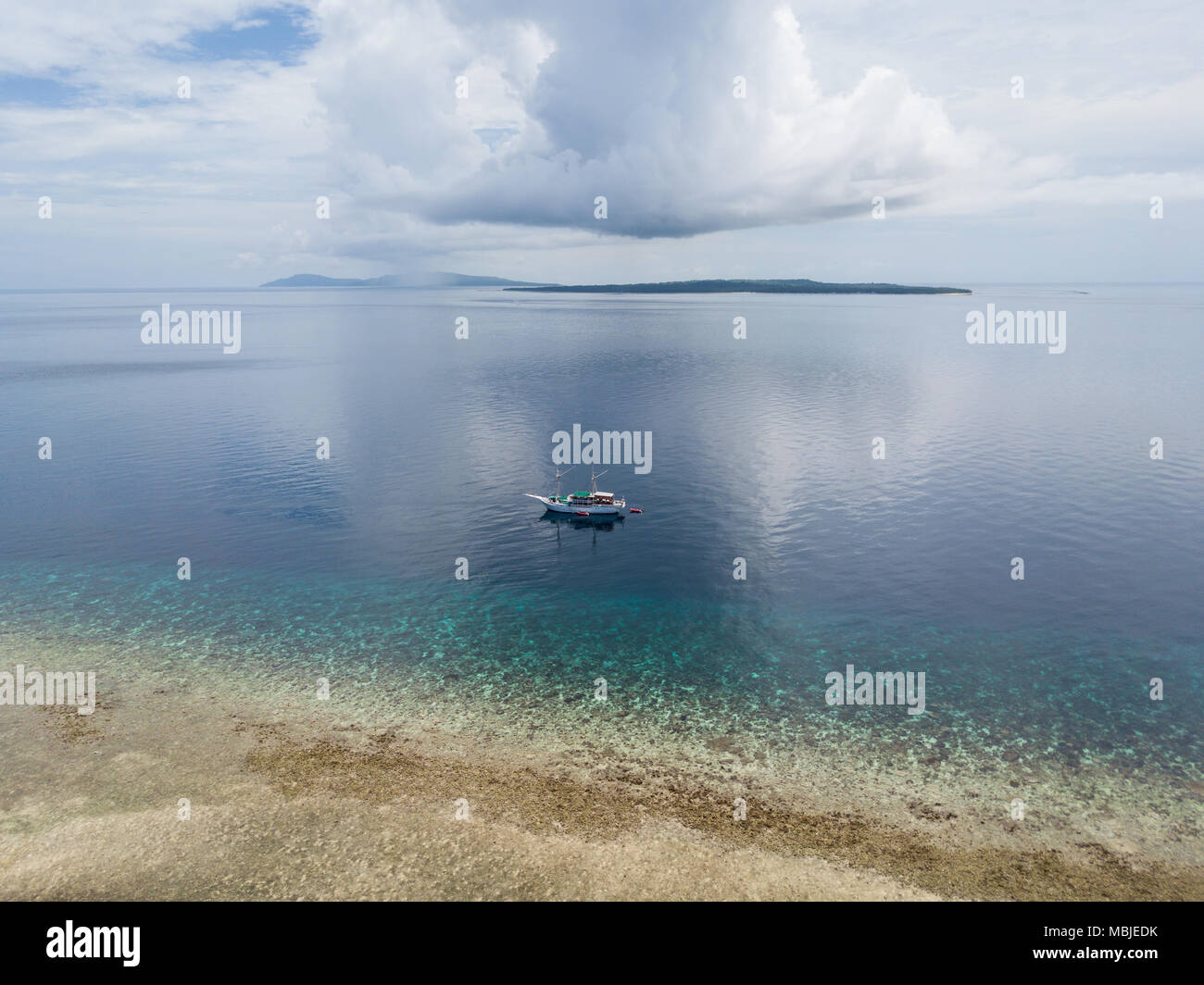 A Pinisi schooner drifts near a remote, tropical island in the Banda