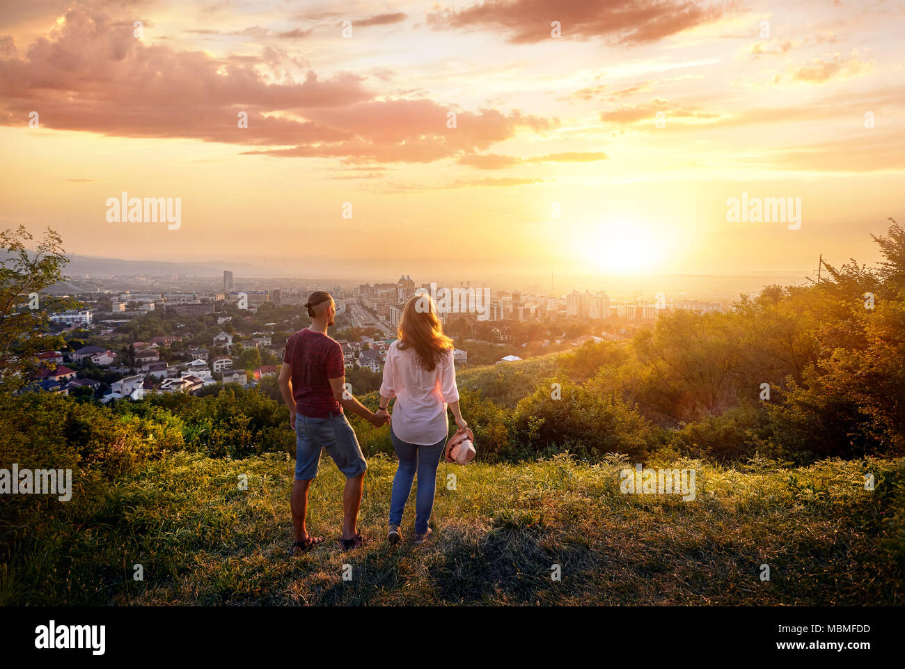 Yong couple in pink clothes holding by hands and looking at the sunset city Stock Photo