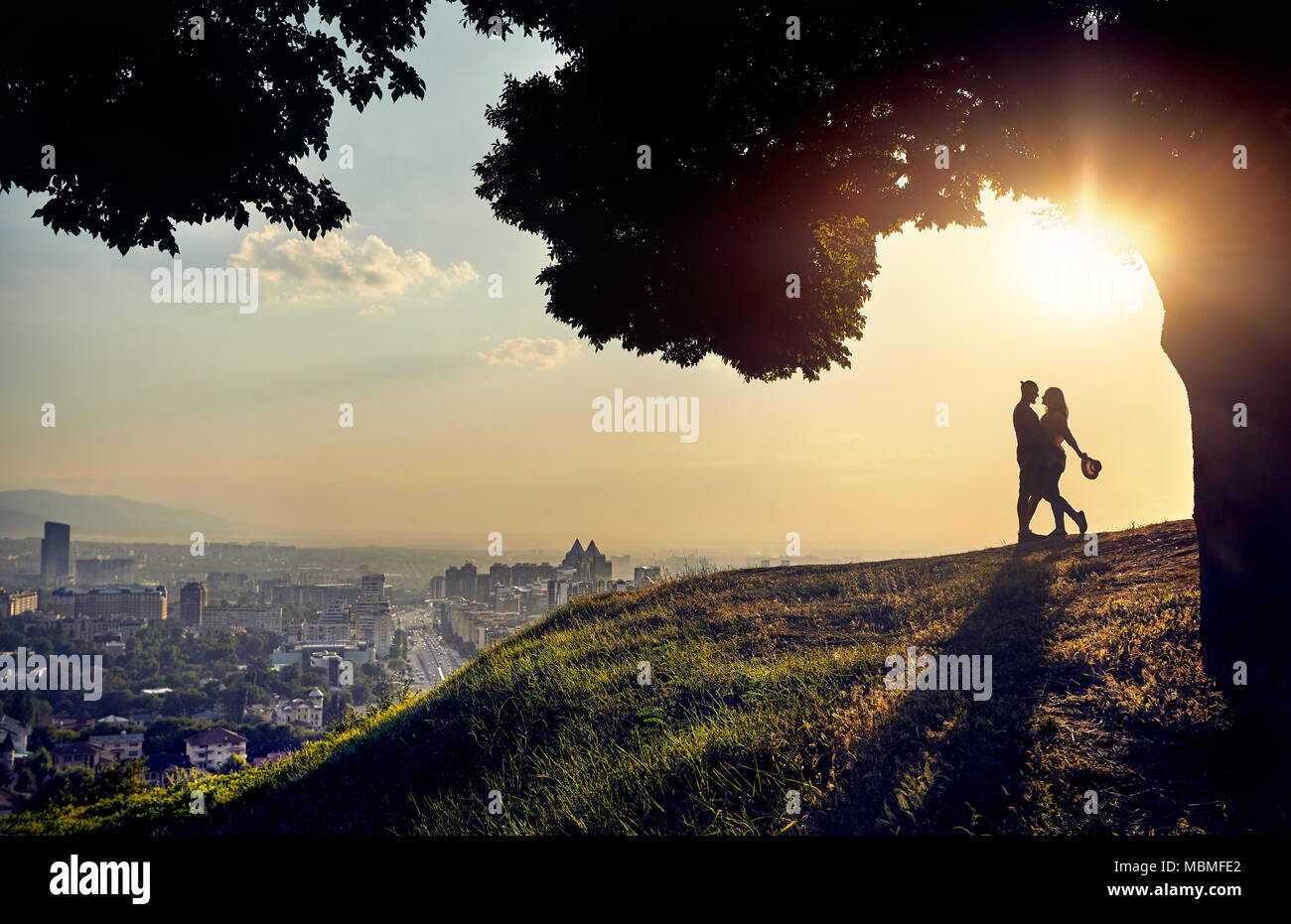 Yong couple in silhouette hugging and looking at the sunset city landscape Stock Photo