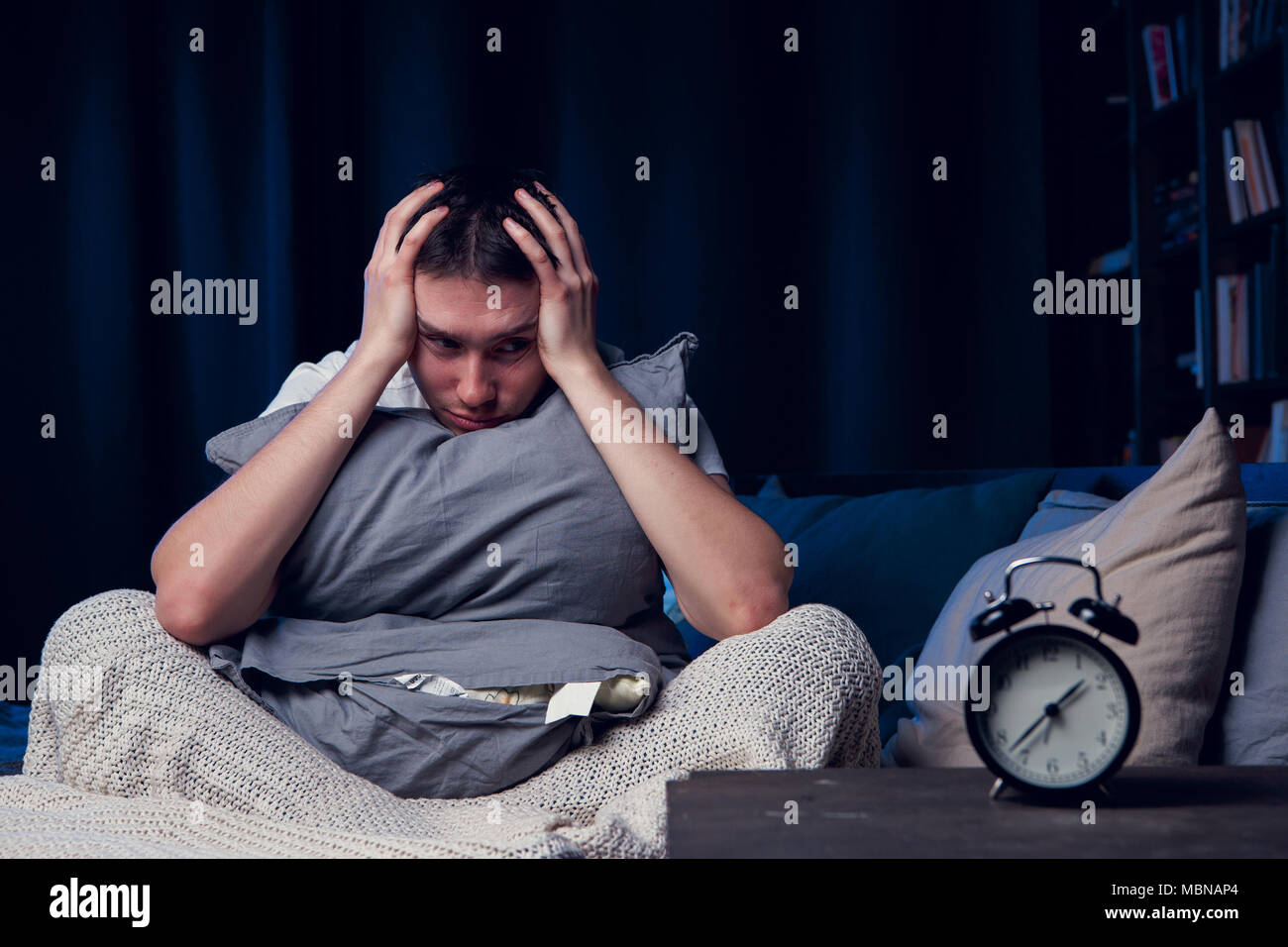 Image of man with insomnia with pillow sitting next to alarm Stock Photo