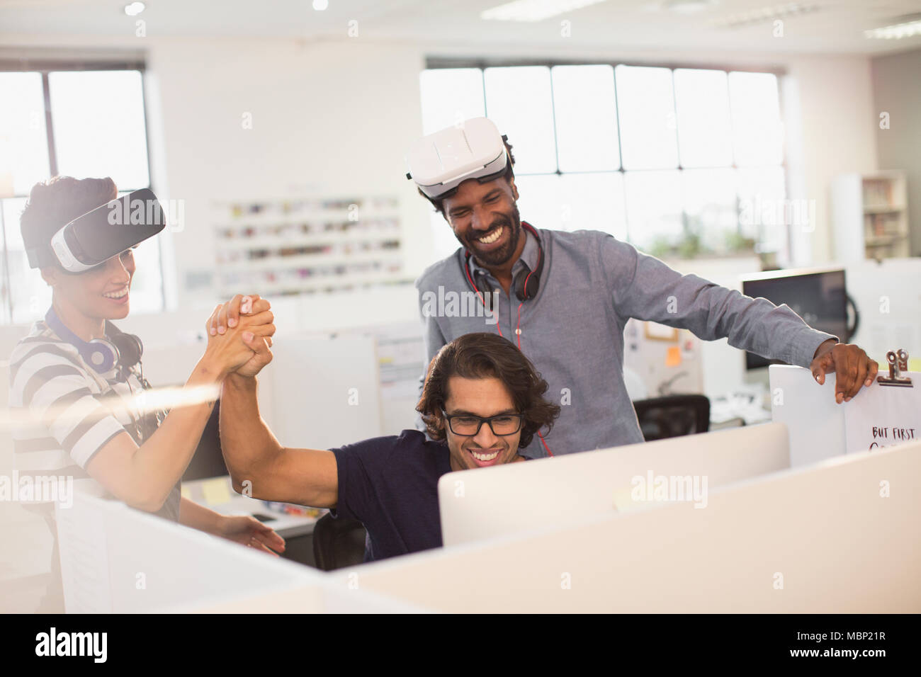 Smiling, enthusiastic computer programmers high-fiving, testing virtual reality simulator glasses Stock Photo