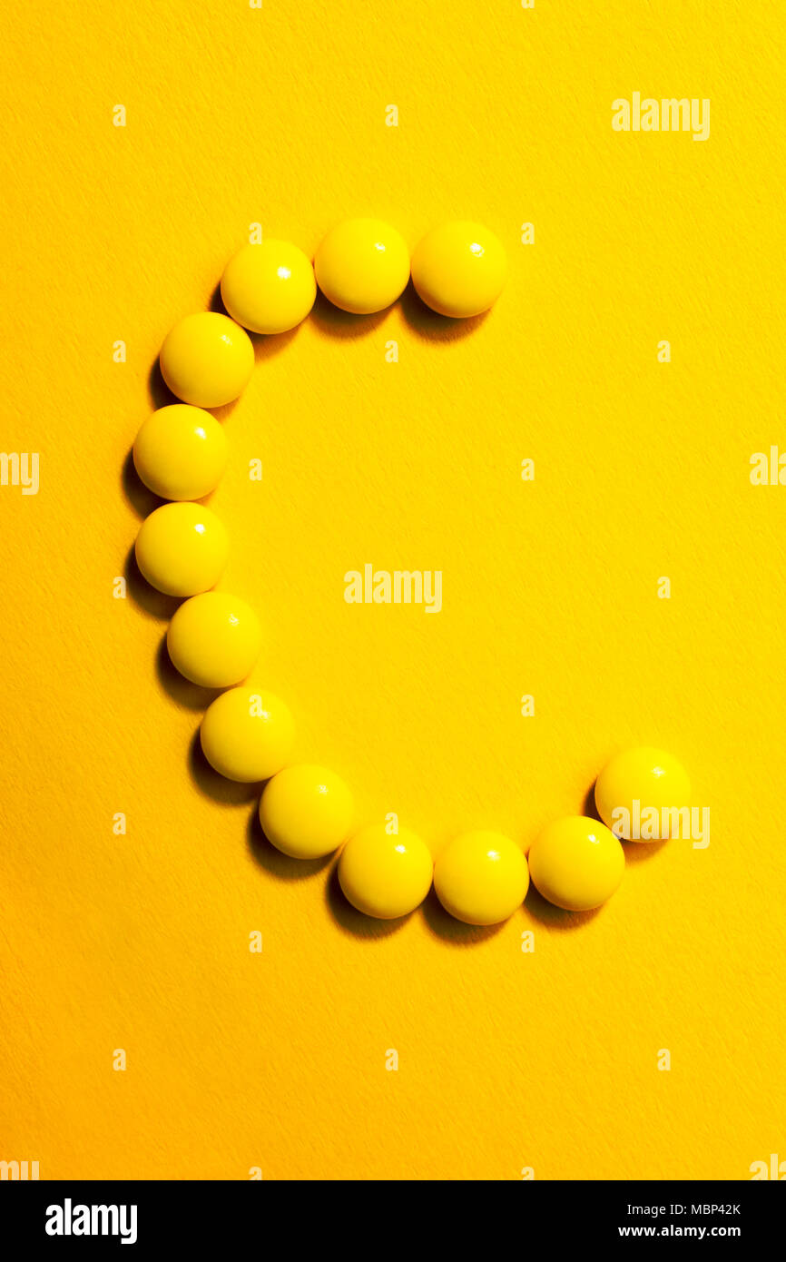 Top view of  letter C made of yellow pills on yellow background. Medicine Vitamin C concept. Stock Photo