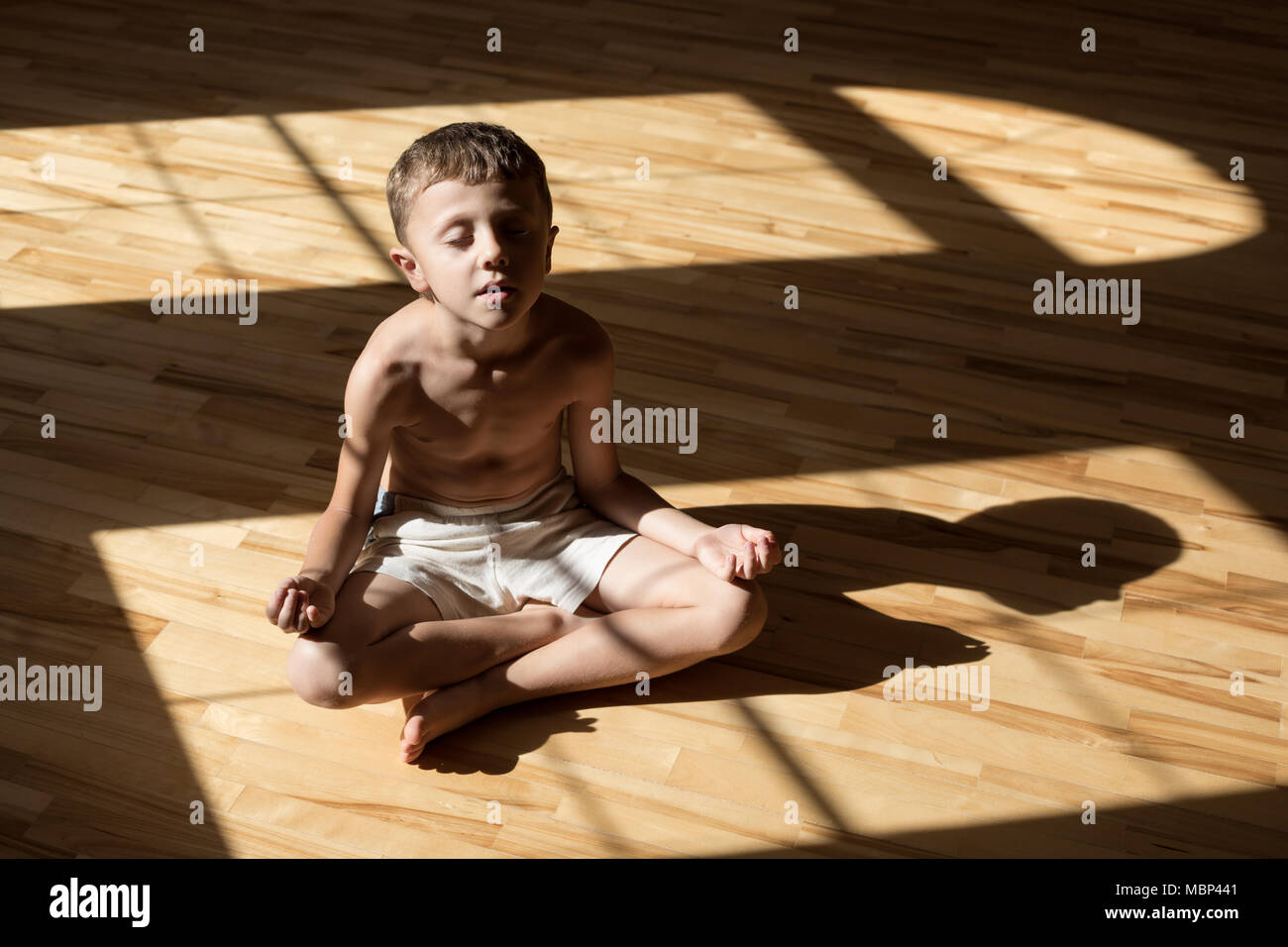 Charming little boy is while doing yoga at home at the day time. Stock Photo