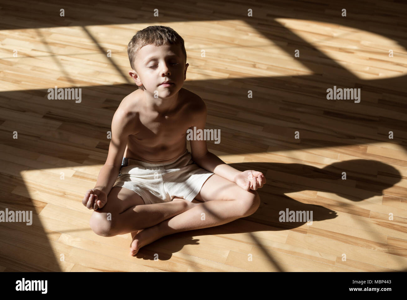 Charming little boy is while doing yoga at home at the day time. Stock Photo