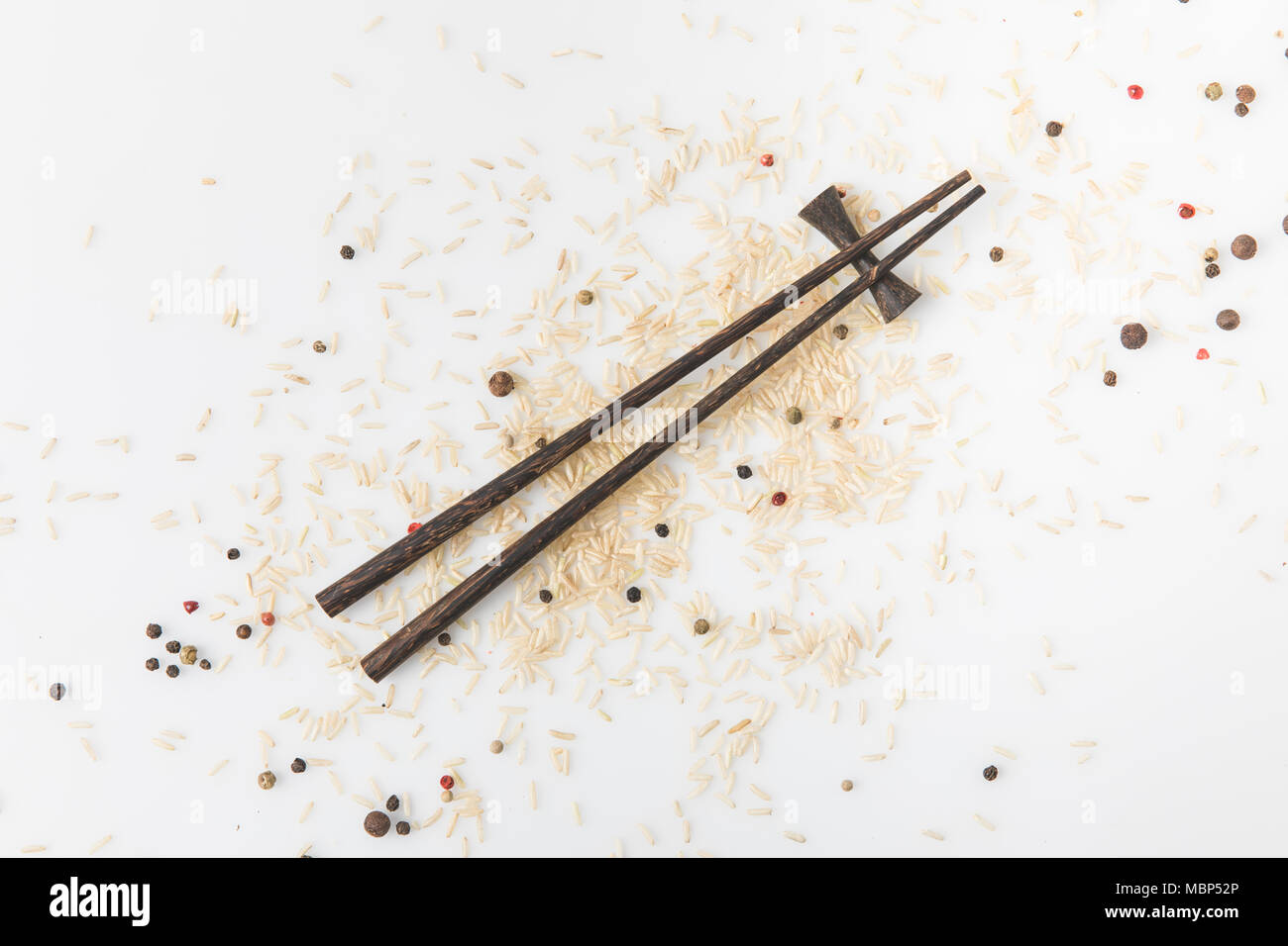 top view of raw rice and spices spilled on white surface with chopsticks Stock Photo