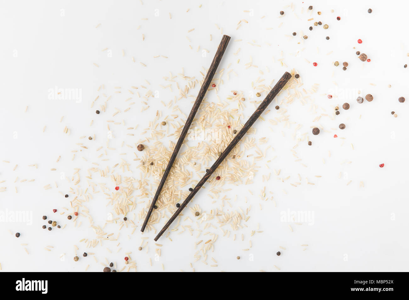 top view of raw rice and spices spilled on white surface with chopsticks Stock Photo