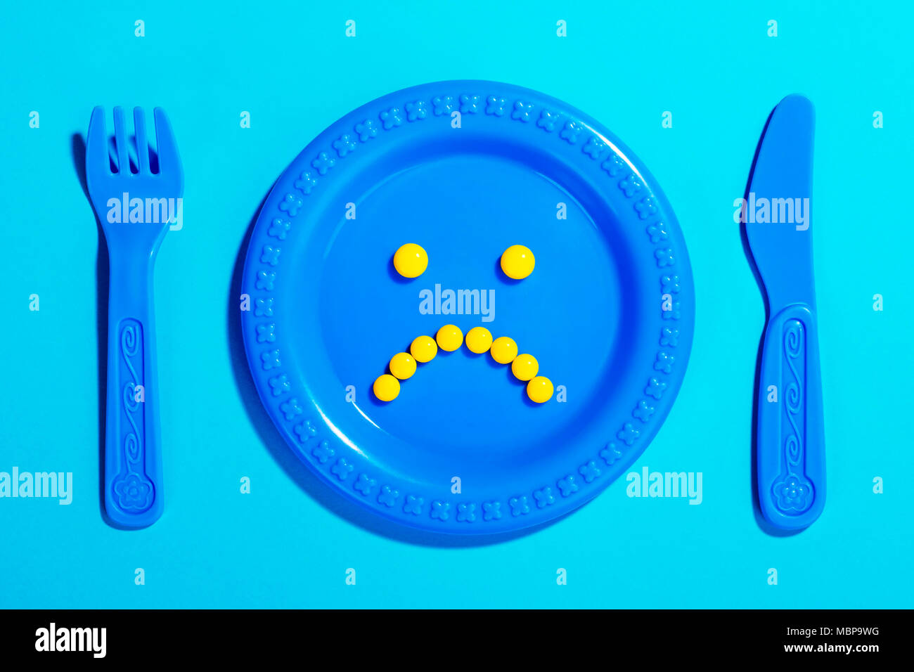 Unhappy face made of yellow pills on children’s plate and cutlery toy. Stock Photo