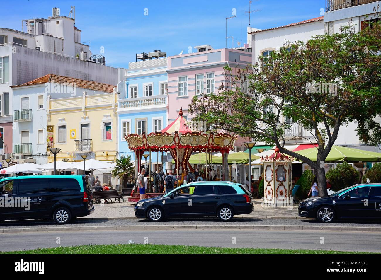 Animal carousel fairground ride along the Rua Porta de Portugal with taxi cabs in the foreground, Lagos, Algarve, Portugal, Europe. Stock Photo