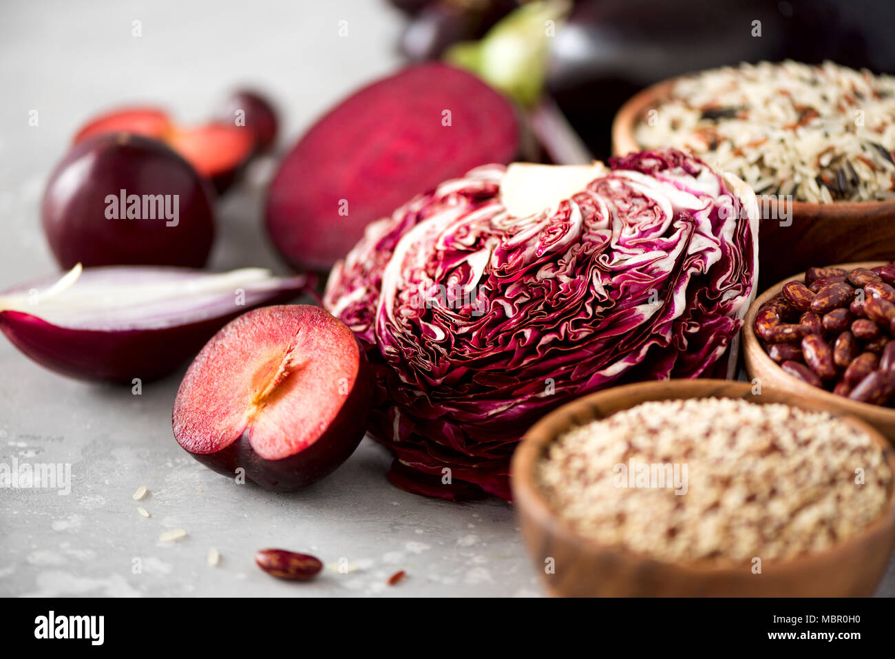 Ingredients for cooking, copy space, top view, flat lay. Purple vegetables, fruits on grey background. Violet eggplant, beets, cauliflower, purple beans, plums, onion, grape, quinoa, rice. Stock Photo