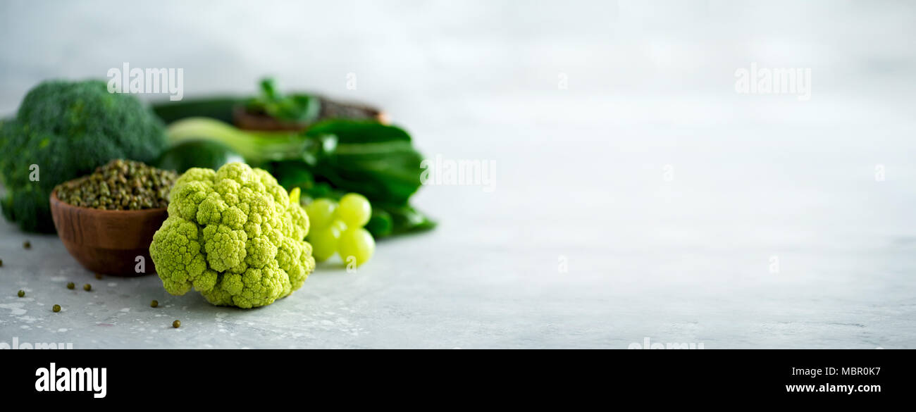 Organic green vegetables and fruits on grey background. Copy space, flat lay, top view. Green apple, avocado, kale, lime, kiwi, grapes, broccoli, marbled lentils, mung bean. Banner Stock Photo