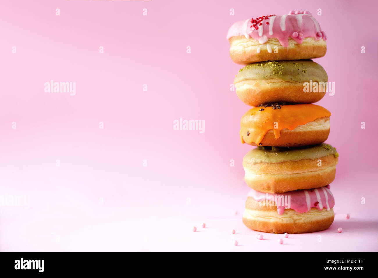 Stack of glazed colorful assorted donuts with sprinkles on pink ...