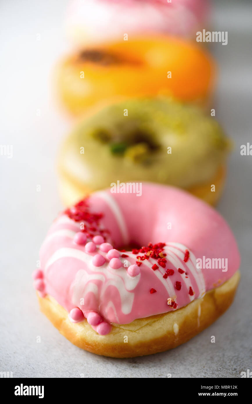 Stack of glazed colorful assorted donuts with sprinkles on grey cement ...