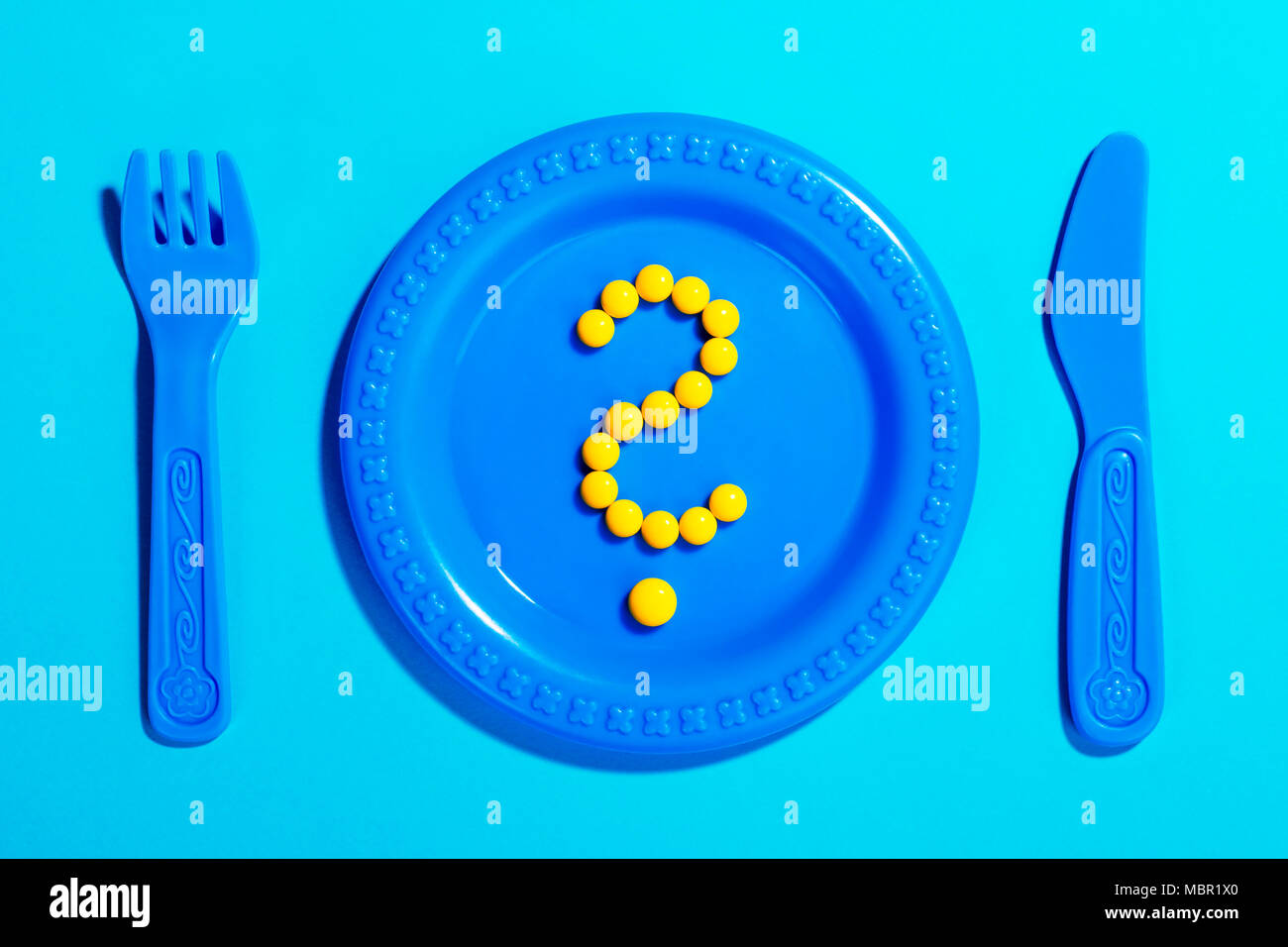 Question mark created from yellow pills on children’s plate and cutlery toy. Medical concept. Stock Photo