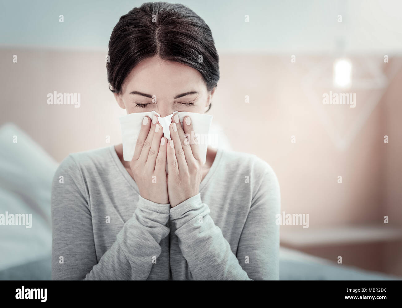 Ill exhausted woman sitting and sneezing. Stock Photo