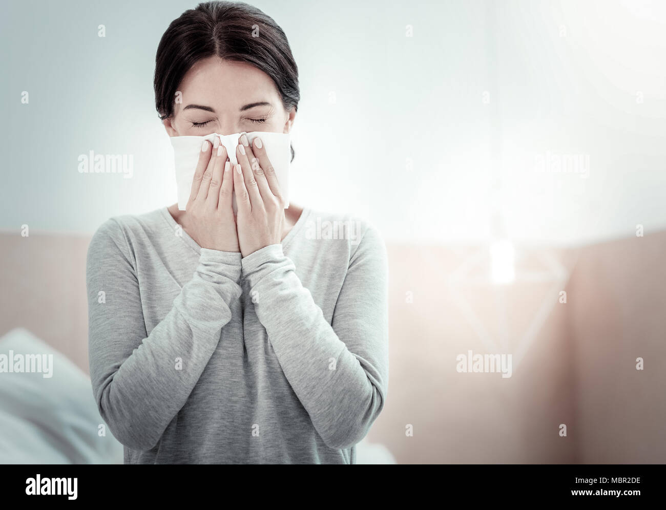 Tired sick woman closing eyes and sneezing. Stock Photo