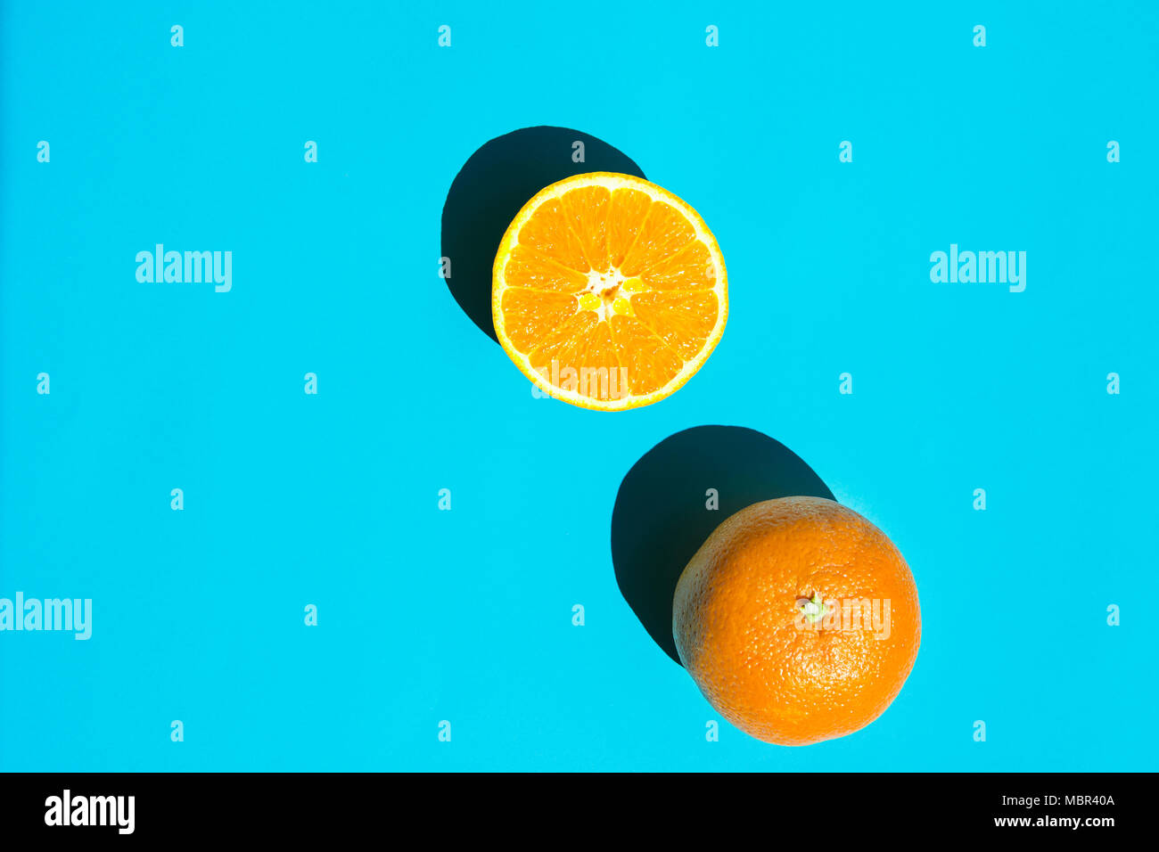 Whole and Halved Ripe Juicy Orange on Blue Background. Bright Harsh Sunlight Deep Shadow. Vibrant Neon Colors. Summer Tropical Vacation Travel Fashion Stock Photo