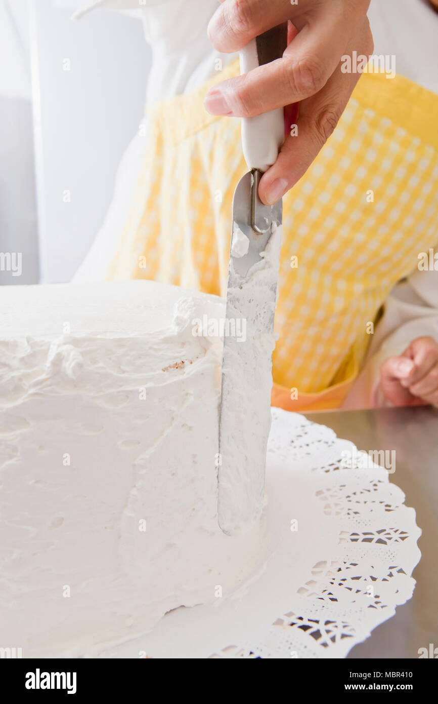 Woman Icing a cake with white cream and a spatula Stock Photo