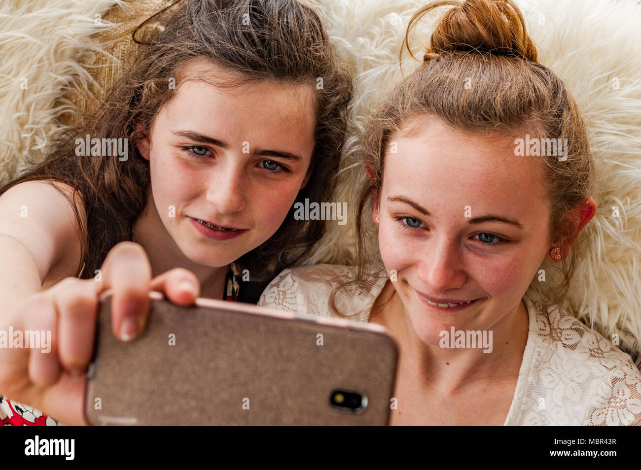Two happy teenage girls taking a selfie indoors with a smartphone. Stock Photo