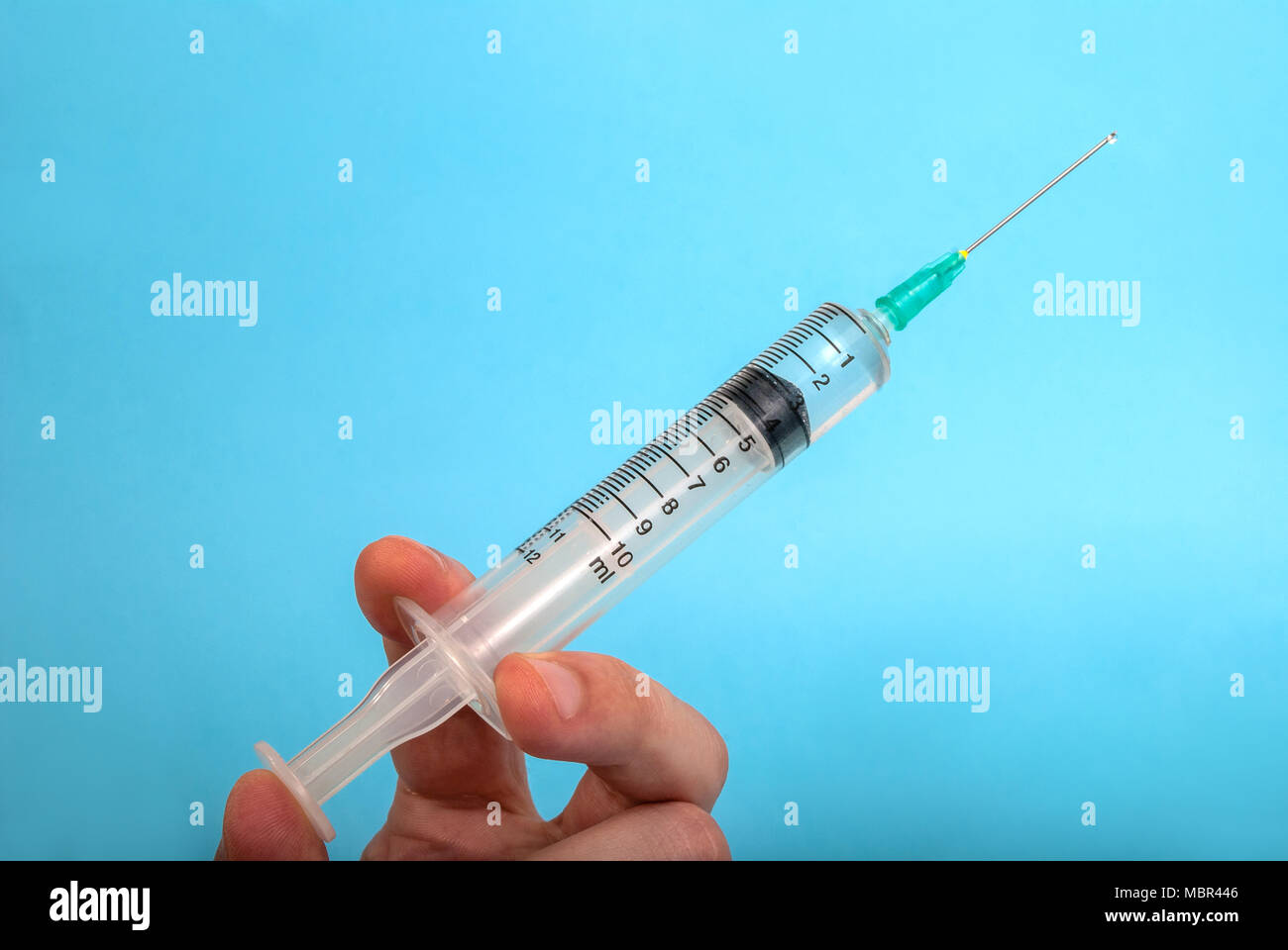 Injection with a needle in the hand without medical gloves and a drop of a drug isolated on a blue background, medical concept Stock Photo