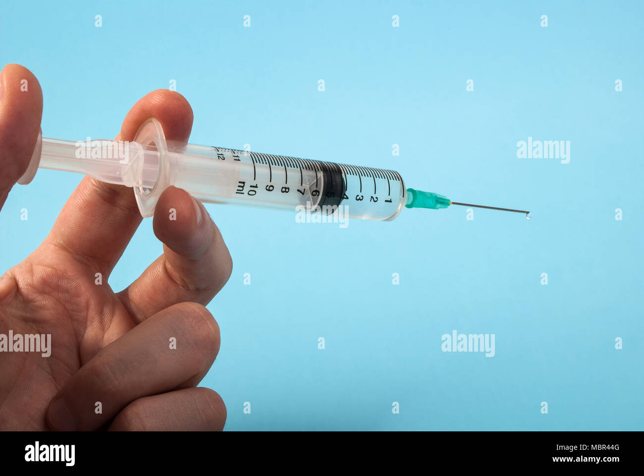 Injection with needle in hand without medical gloves isolated on blue background, medical concept Stock Photo