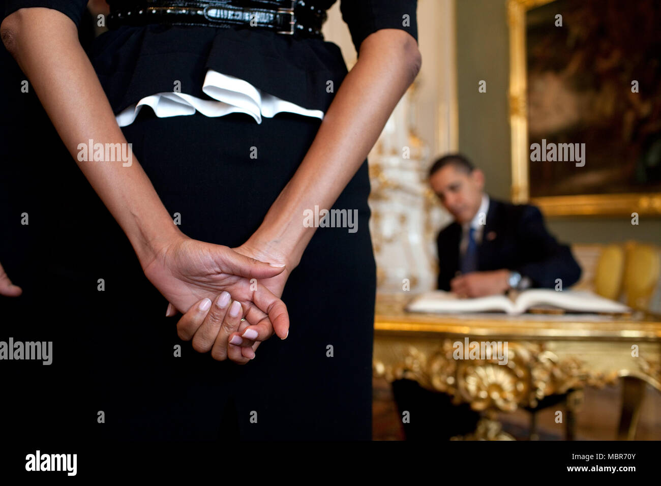 First Lady Michelle Obama waits as President Barack Obama, background, signs the guestbook upon their arrival to Prague Castle,  April 5, 2009, in the Czech Republic. White House Photo/Pete Souza Stock Photo
