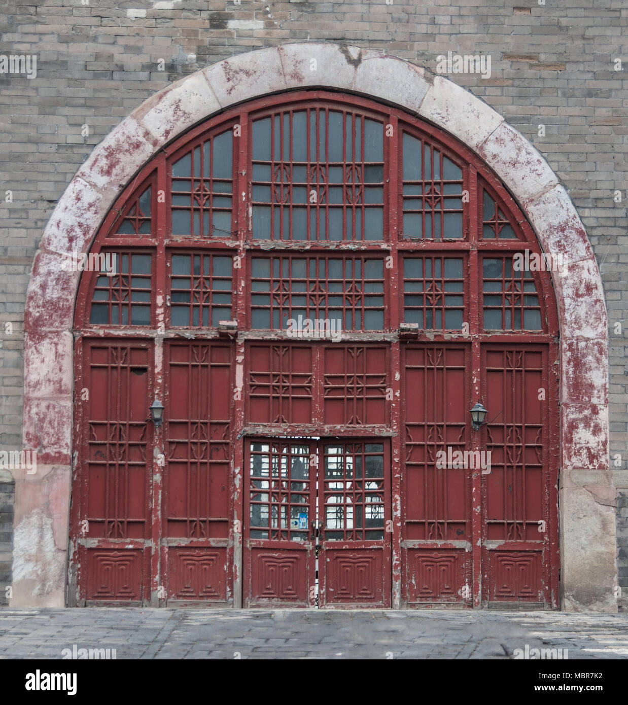 Beijing, China - April 26, 2010: Closeup of large bow-shaped maroon entrance door to under-belly of Bell Tower set in gray stone wall. Stock Photo