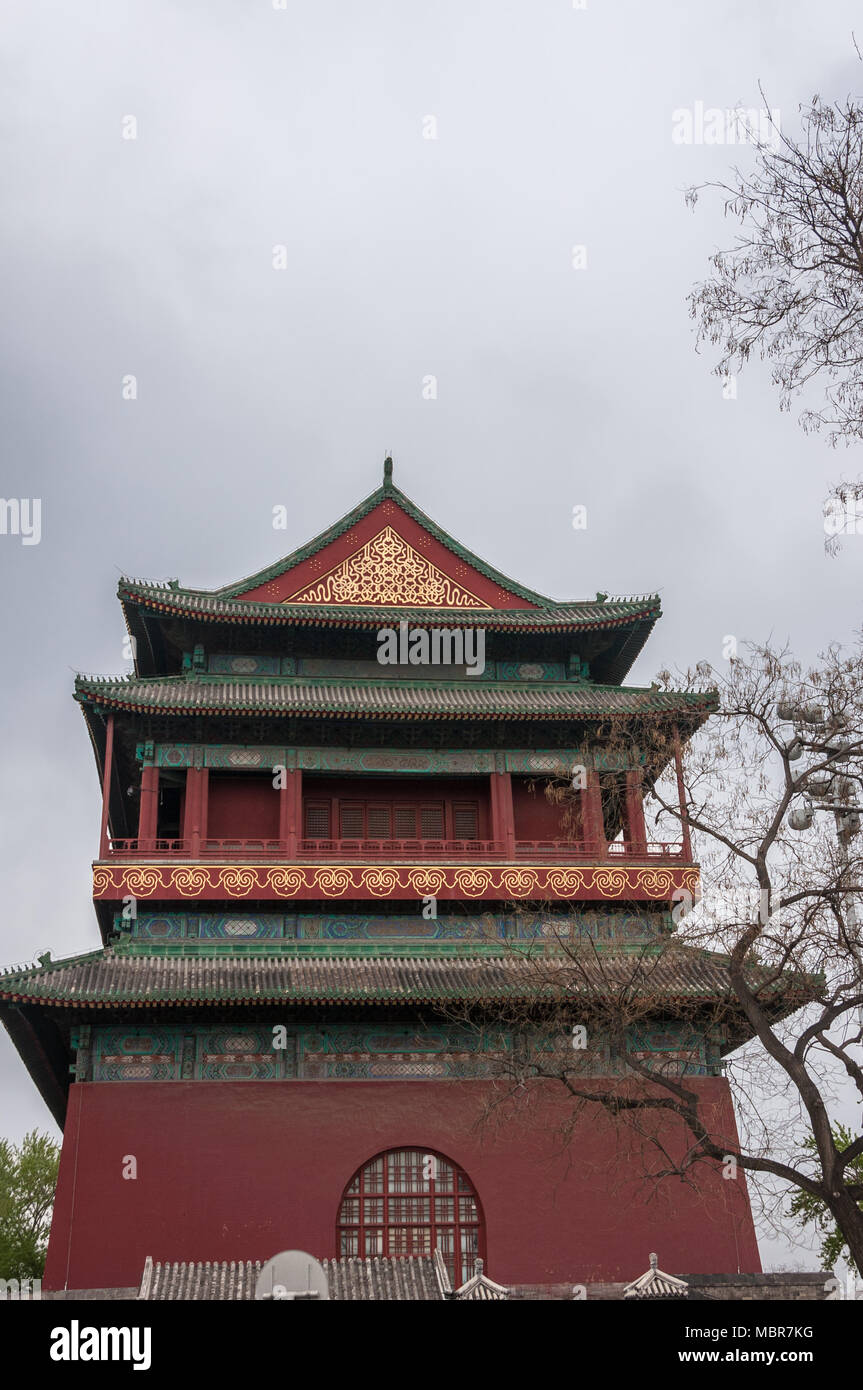 Beijing, China - April 26, 2010: Short side of upper structure of Drum Tower shows maroon, green and gold colors under gray sky. Some tree in photo. Stock Photo