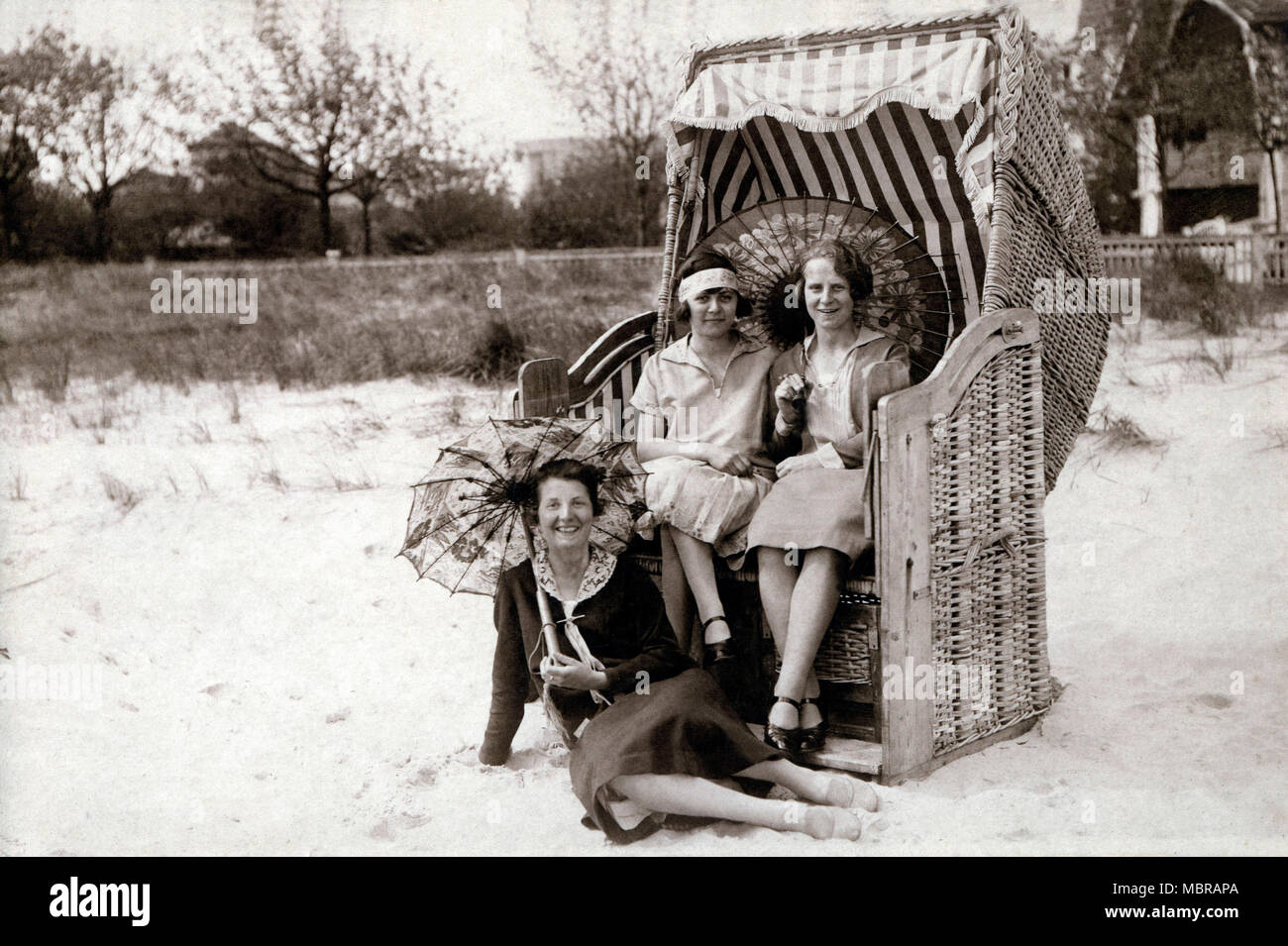 Three women on the beach, two sitting in beach chairs with sunshades ...